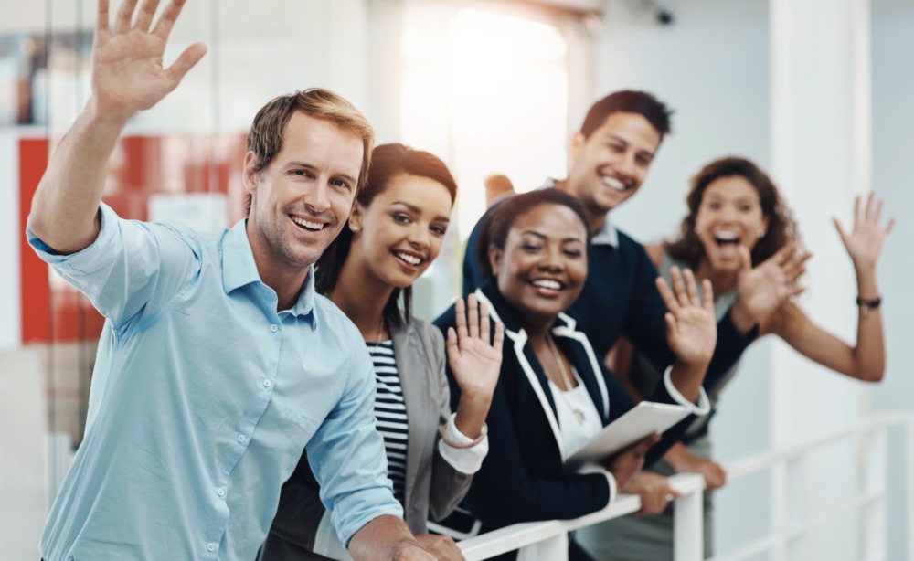 Diverse group of business professionals smiling and waving in a modern office setting