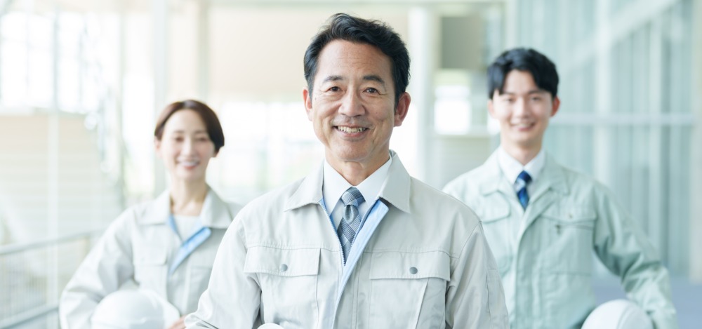 Three Japanese manufacturing professionals smiling confidently in work uniforms, symbolizing success in global business expansion.