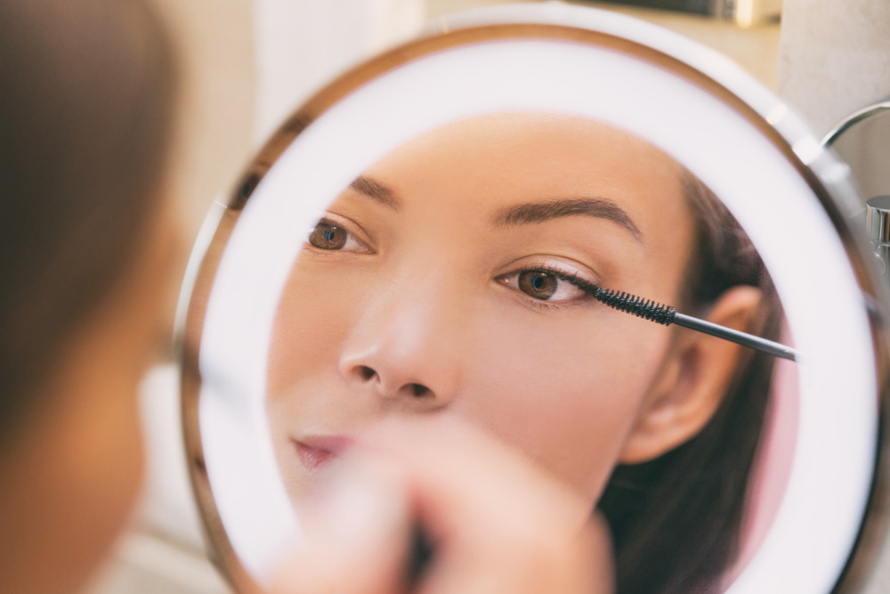 Close-up of a woman applying mascara in front of a ring light mirror, representing Singapore’s dynamic beauty and cosmetics market