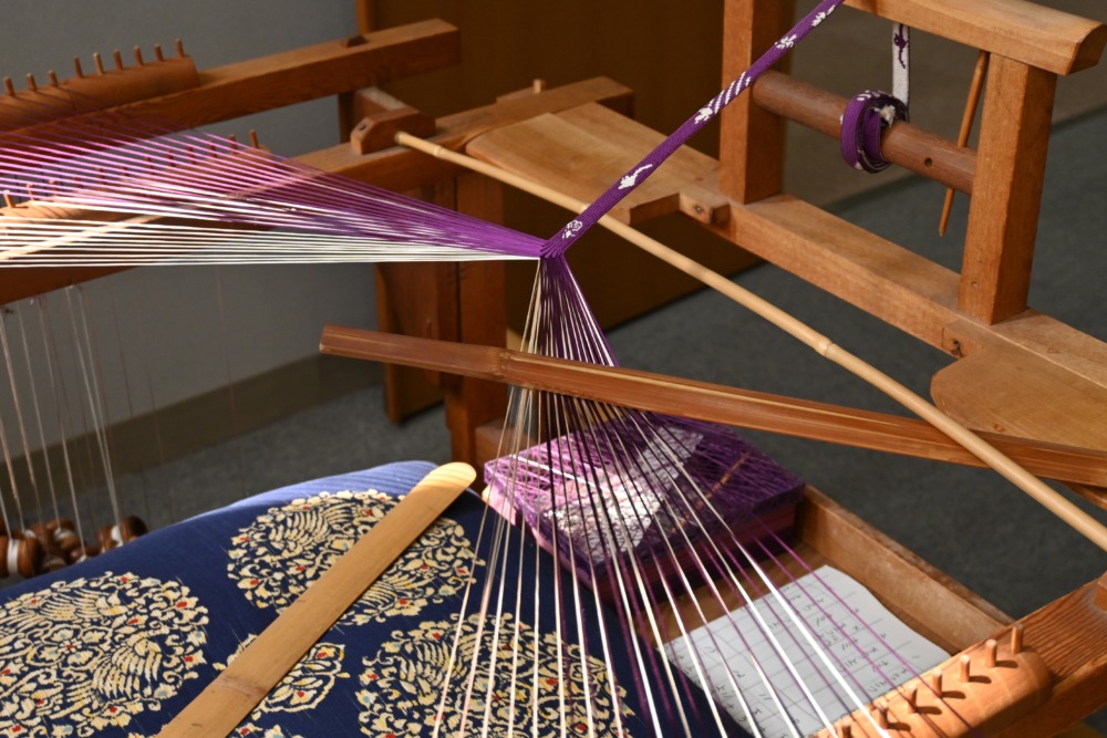Traditional Nishijin textile weaving loom with purple threads in production process